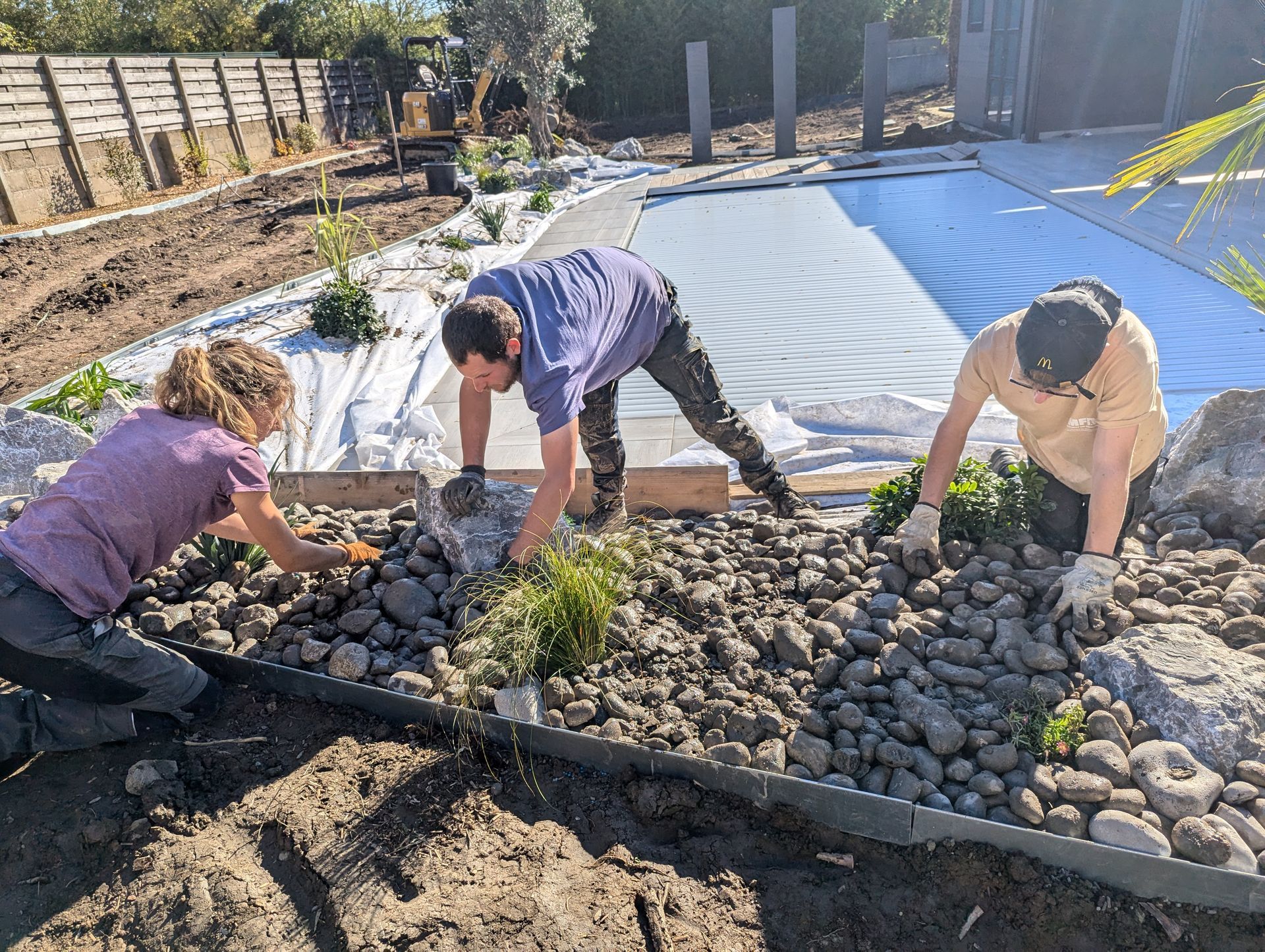 3 paysagistes travaillant sur l'aménagement paysager du terrain autour d'une piscine