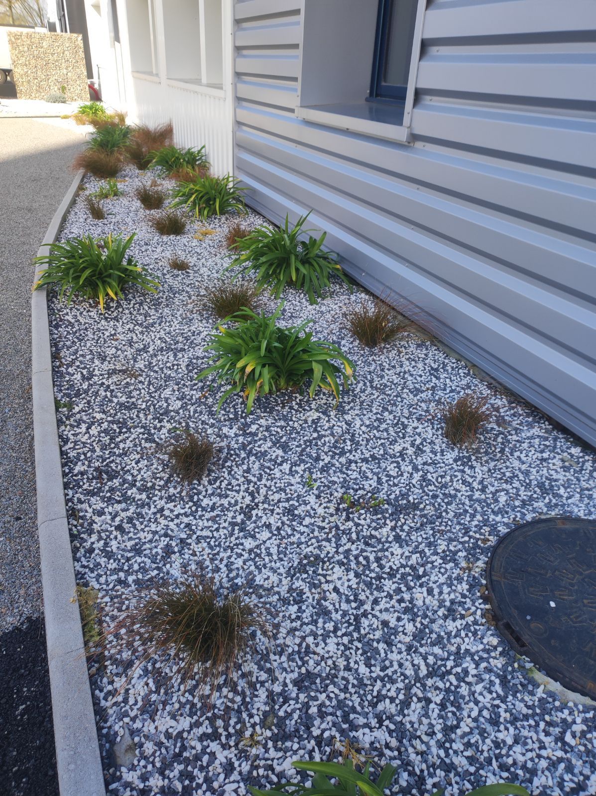 Massif paysager avec de petites plantations installées le long du bardage en métal d'une entreprise