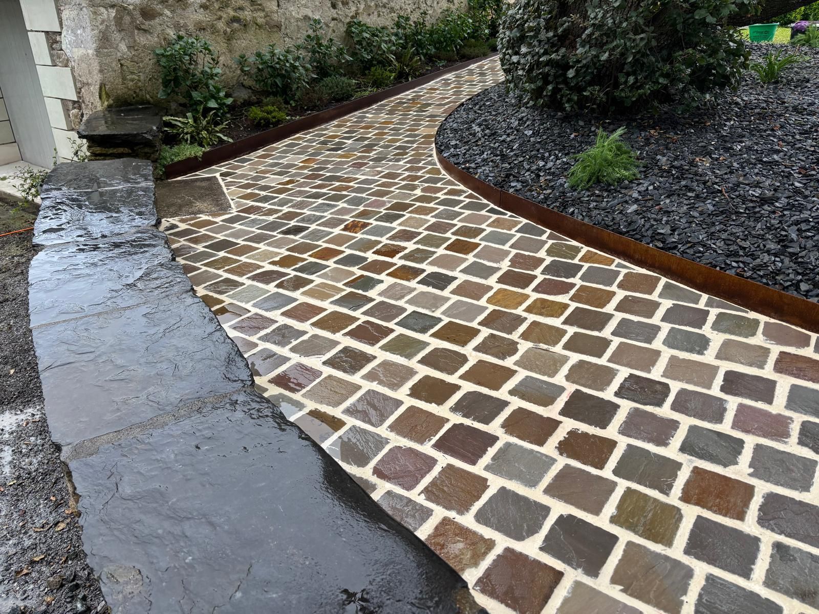 Aménagement d'une allée en pavé de pierres aux teintes multiples autour d'un massif paysager