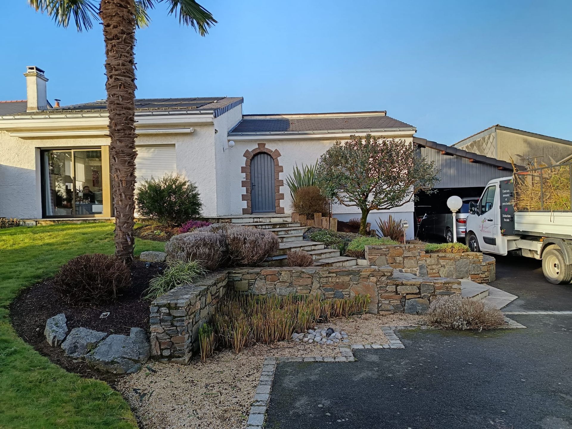 Entretien d'un massif paysager sur plusieurs niveaux avec un palmier en façade d'une maison