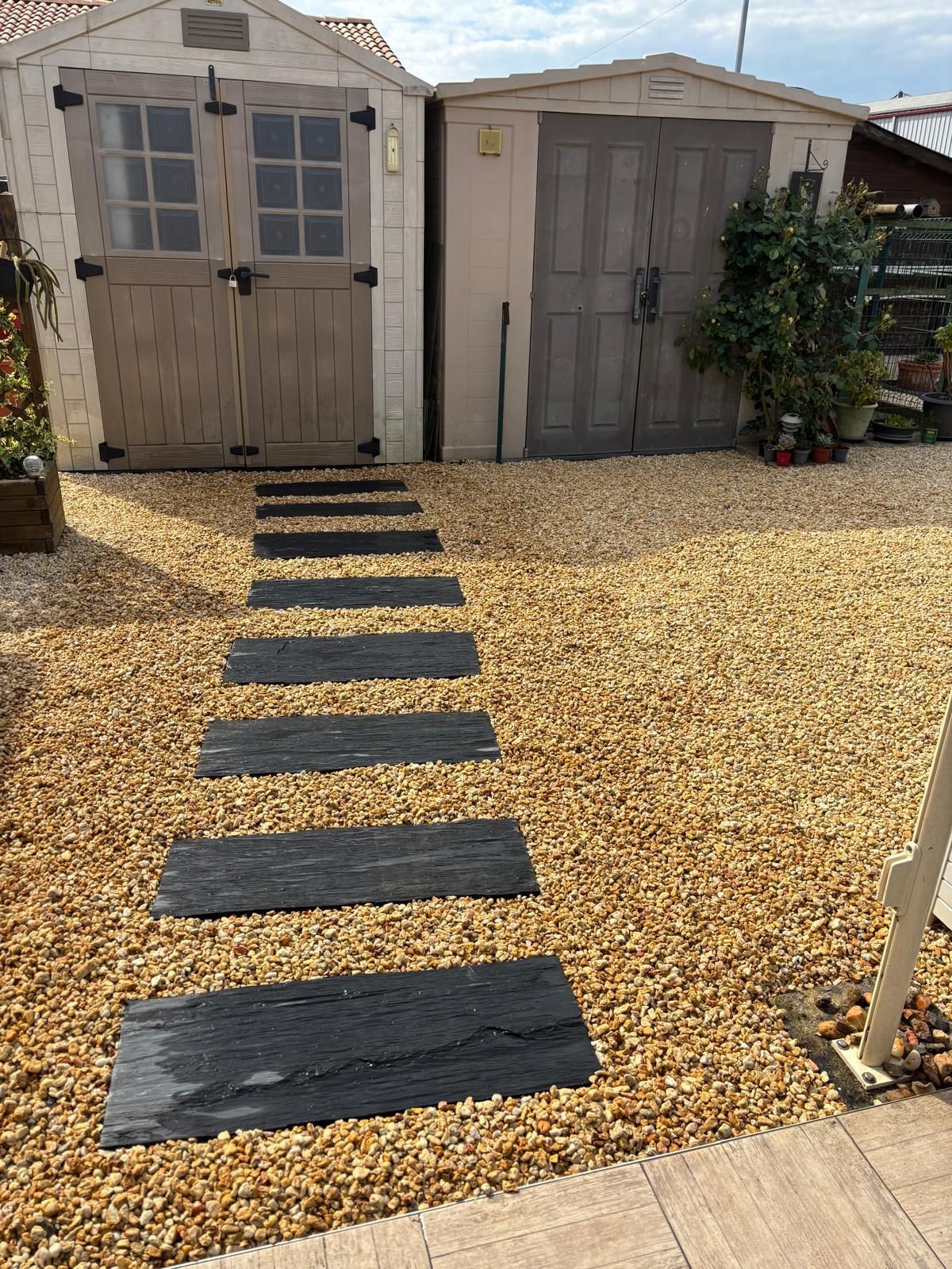 Installation de dalles en pierre et de gravier devant des abris de jardin