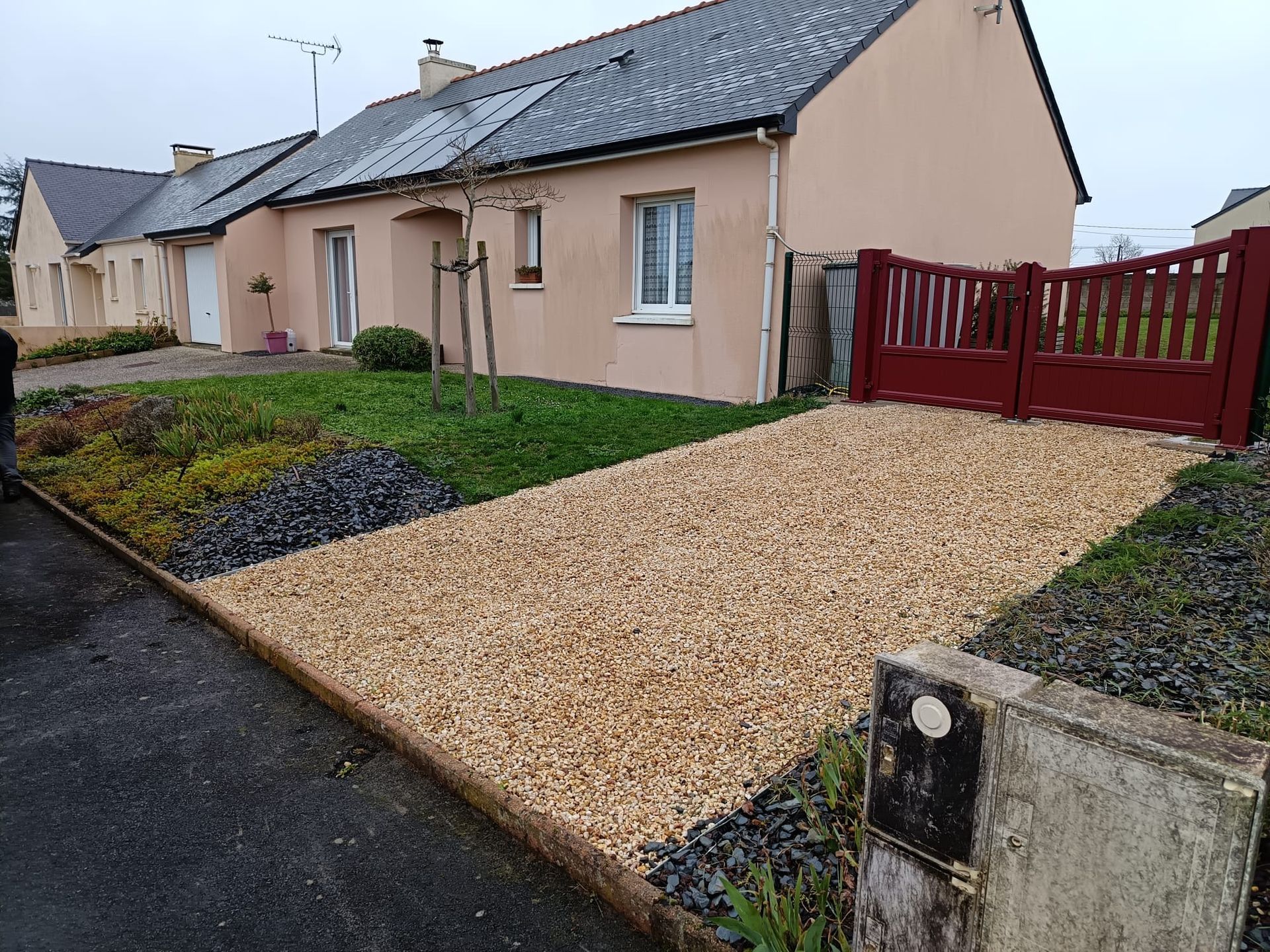 Pose de nidagravel devant le portail rouge d'une maison individuelle