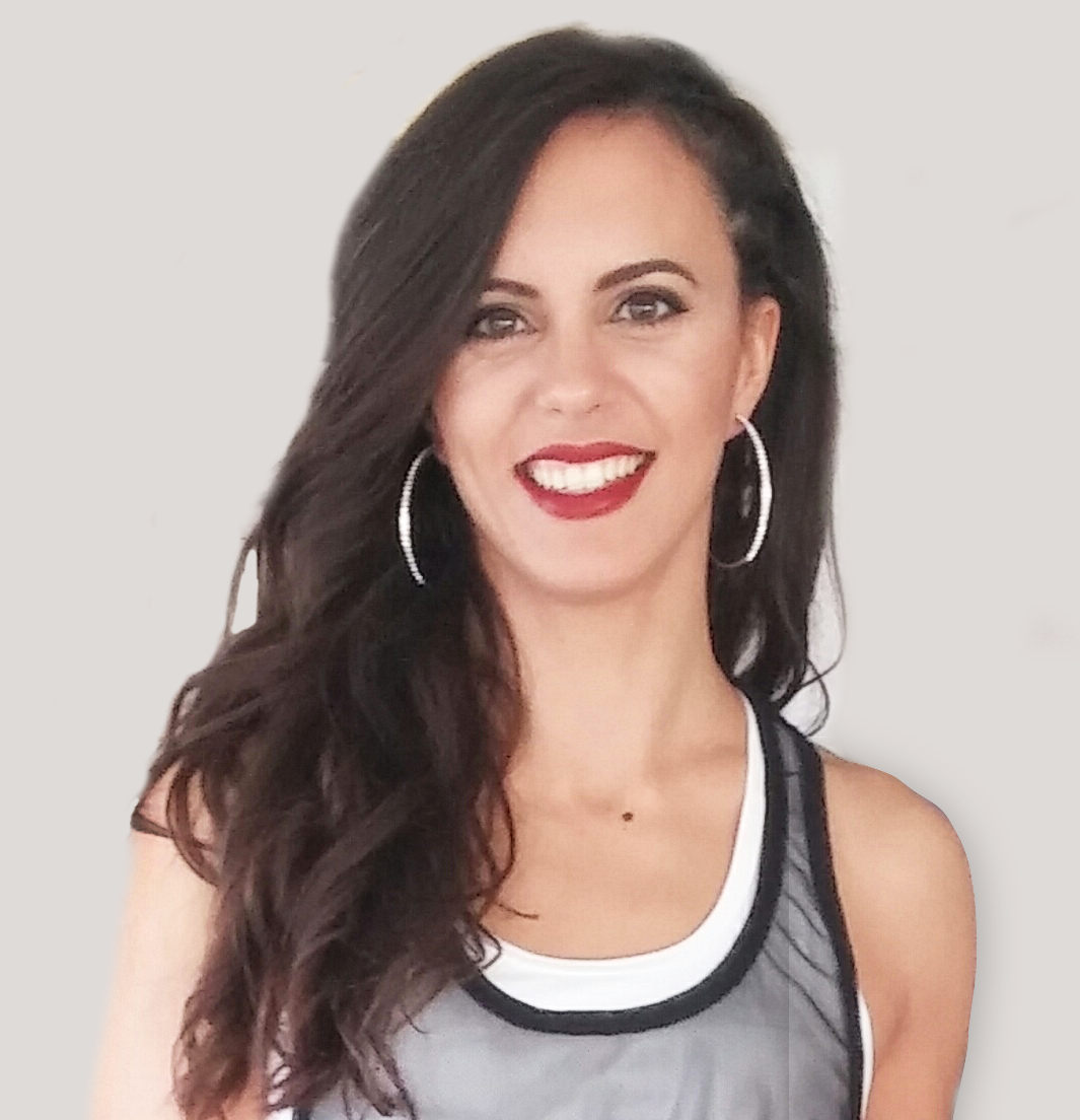 Una mujer con cabello largo y oscuro sonríe, lleva aros y una camiseta deportiva sobre un fondo neutro.