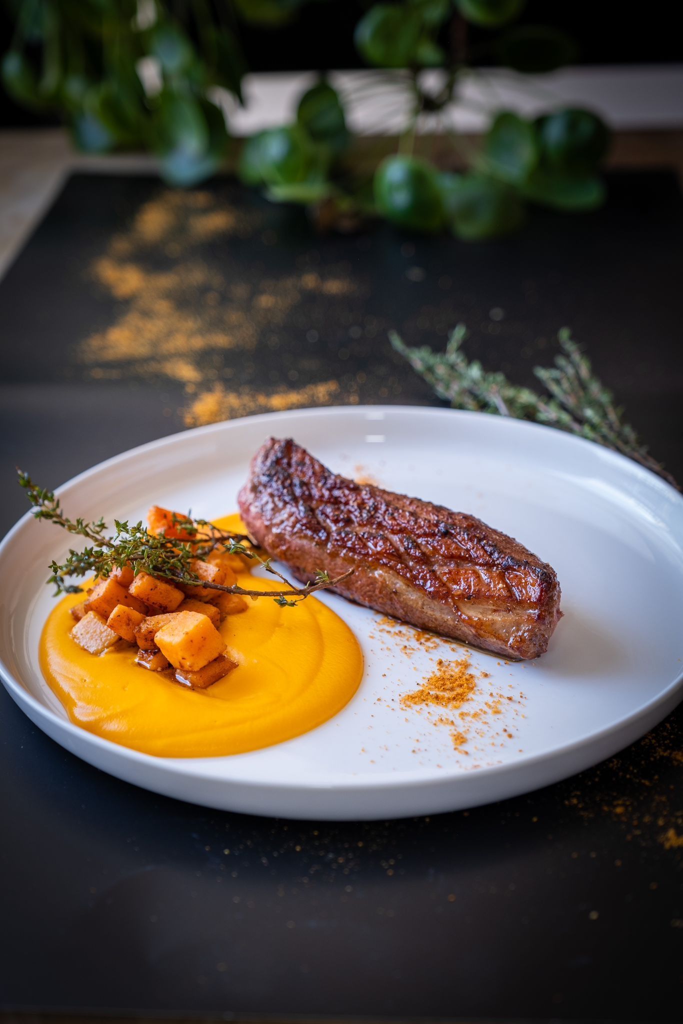 Steak servi avec purée d'oranges et légumes rôtis sur une assiette blanche.