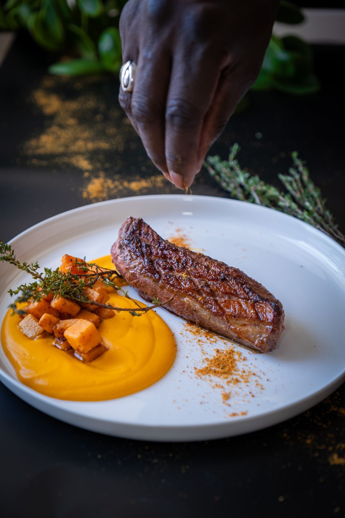Dressage à la main d'un steak saisi sur une assiette blanche avec purée d'orange et herbes.