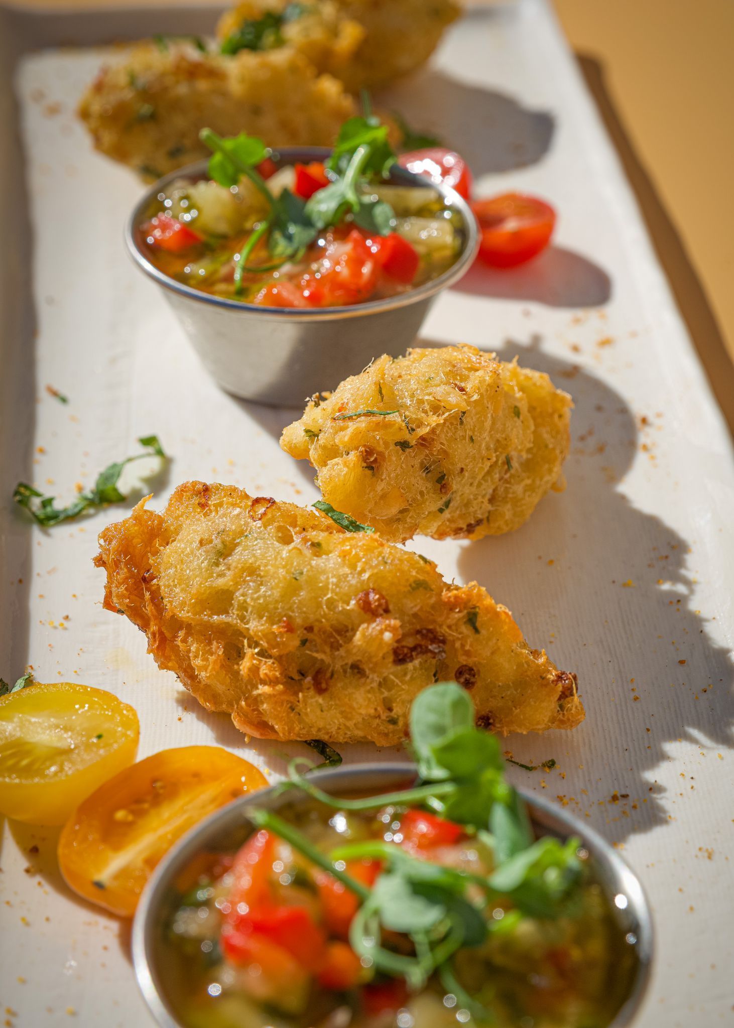 Amuse-gueules panés avec salsa colorée et micro-pousses sur une assiette blanche.