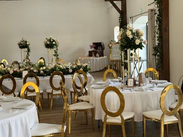 Salle de banquet décorée avec des tables rondes blanches, des chaises dorées et de hauts centres de table floraux.