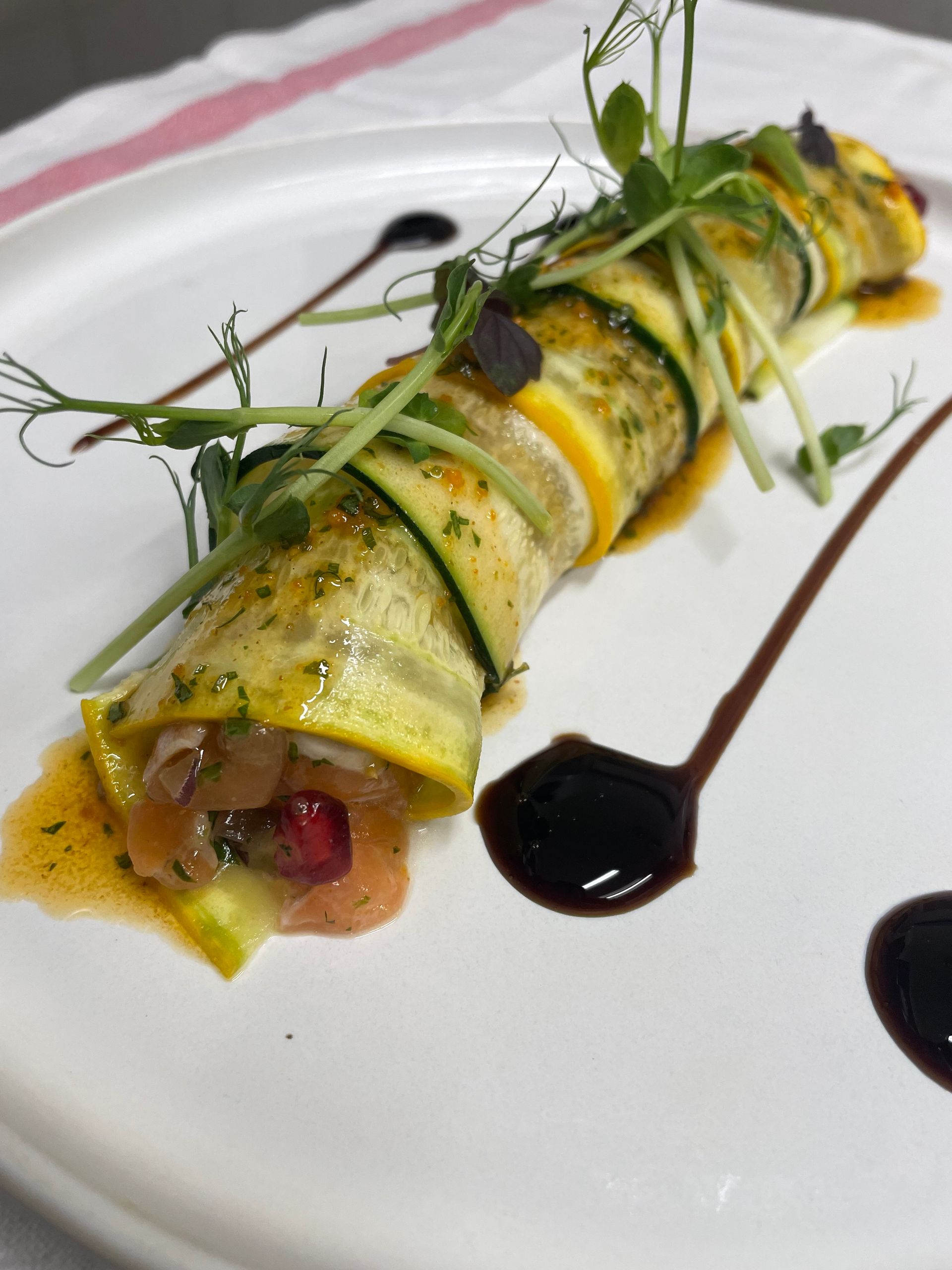 Rouleau de pâtes gastronomique présenté dans une assiette, garni d'herbes et d'un filet de sauce brune.
