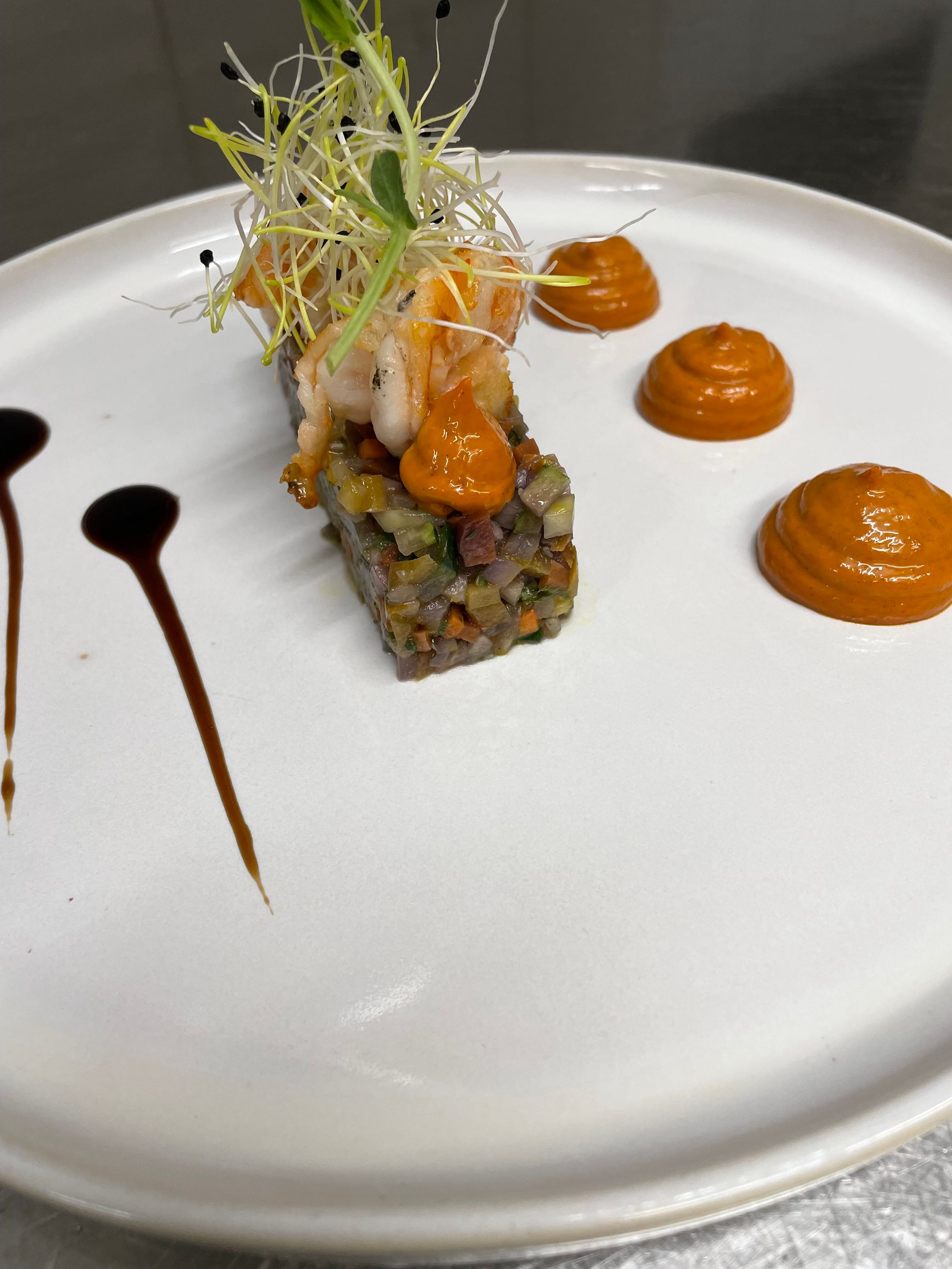 Assiette d'entrée raffinée composée de tartare en dés, de salade verte, de quenelles de sauce à l'orange et d'un filet de vinaigre balsamique foncé, le tout servi sur une assiette blanche.