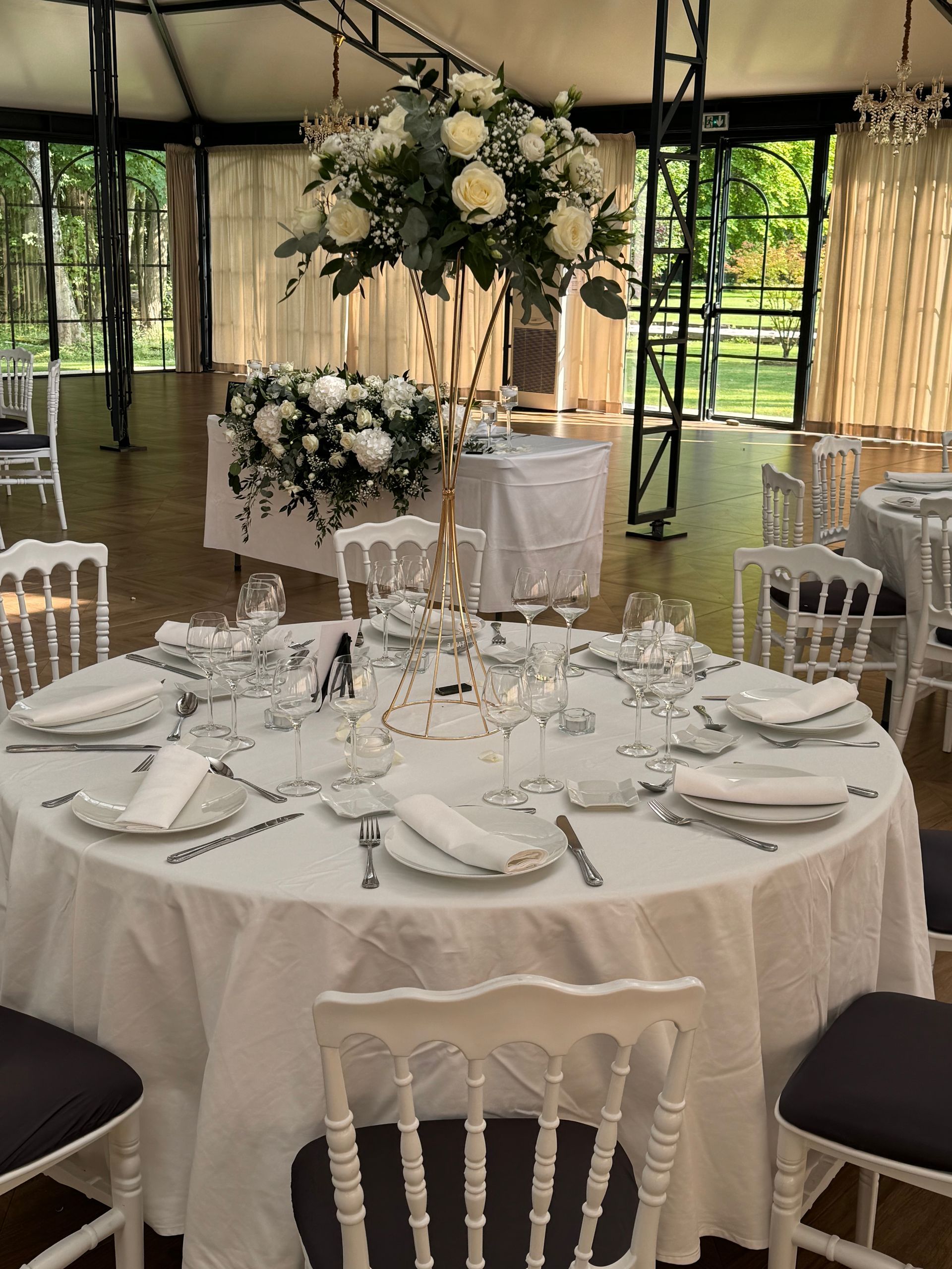 Élégante table ronde de banquet avec nappes blanches, centre de table floral et lustres sous une tente de réception décorée.