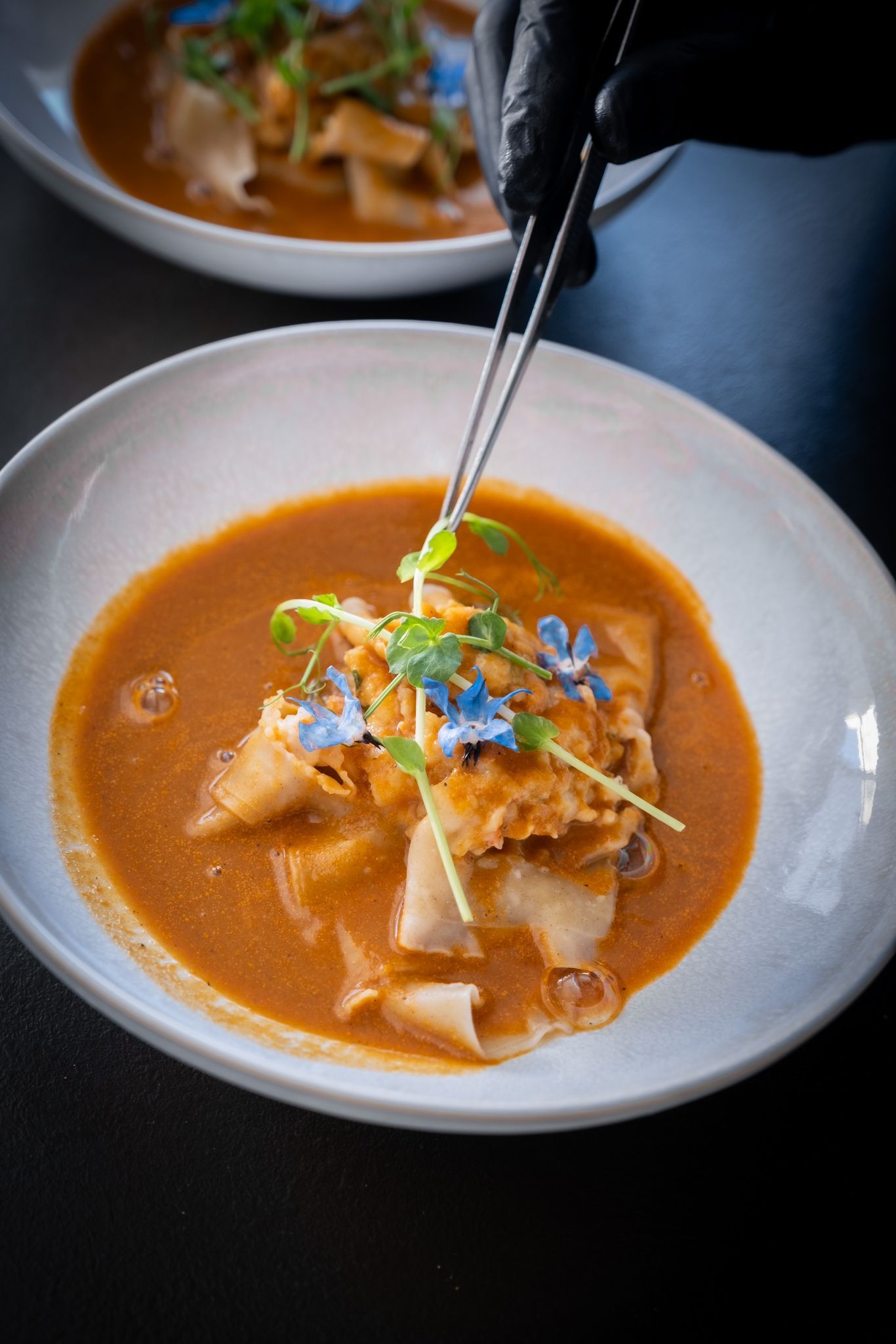 Bol blanc de soupe orange avec garnitures et baguettes noires soulevant les nouilles.