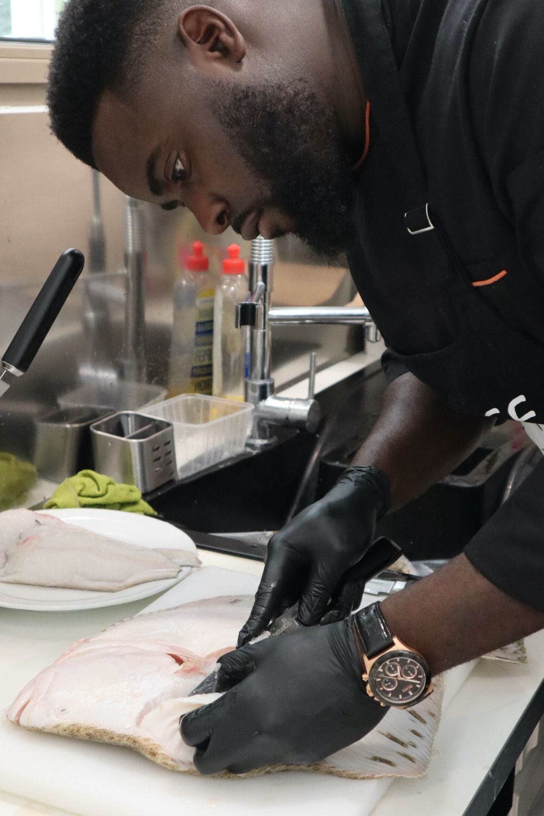 Un chef lève les filets d'un gros poisson sur une planche à découper dans la zone de préparation de la cuisine.