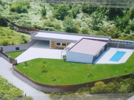 Casa moderna con techos planos y piscina, situada en una colina cubierta de hierba con árboles circundantes.