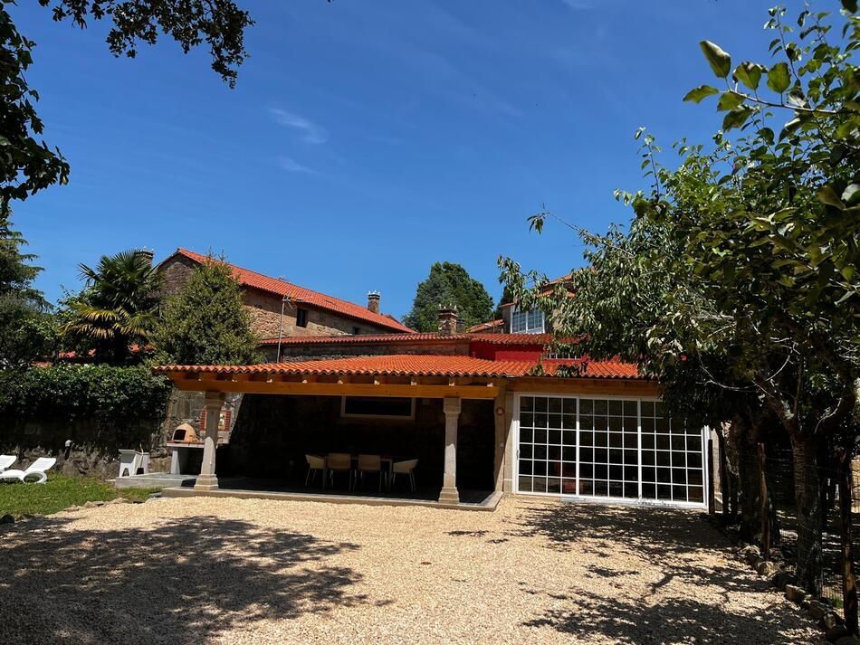 Casa de piedra con patio cubierto y ventanas de cristal bajo un cielo azul claro.