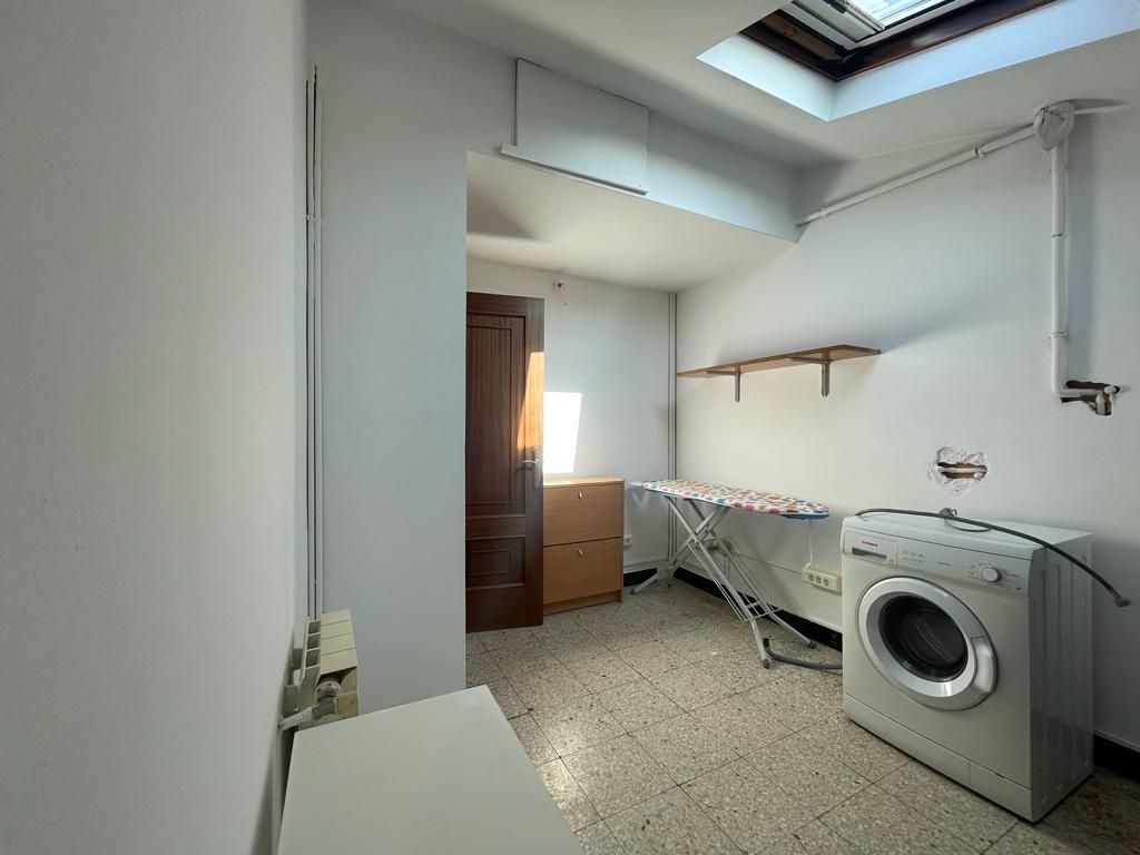 Lavandería con lavadora, tabla de planchar y estanterías.