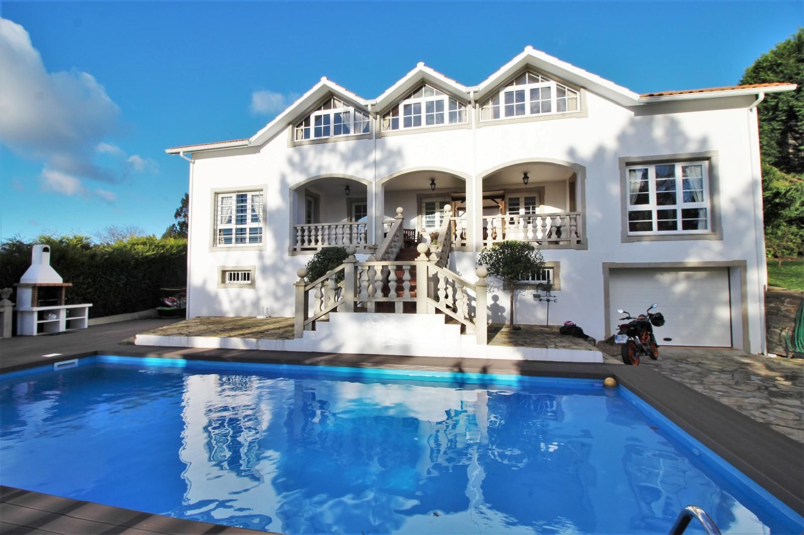 Casa blanca con piscina y cielo azul. Escaleras que conducen al balcón. Parrilla en el patio.