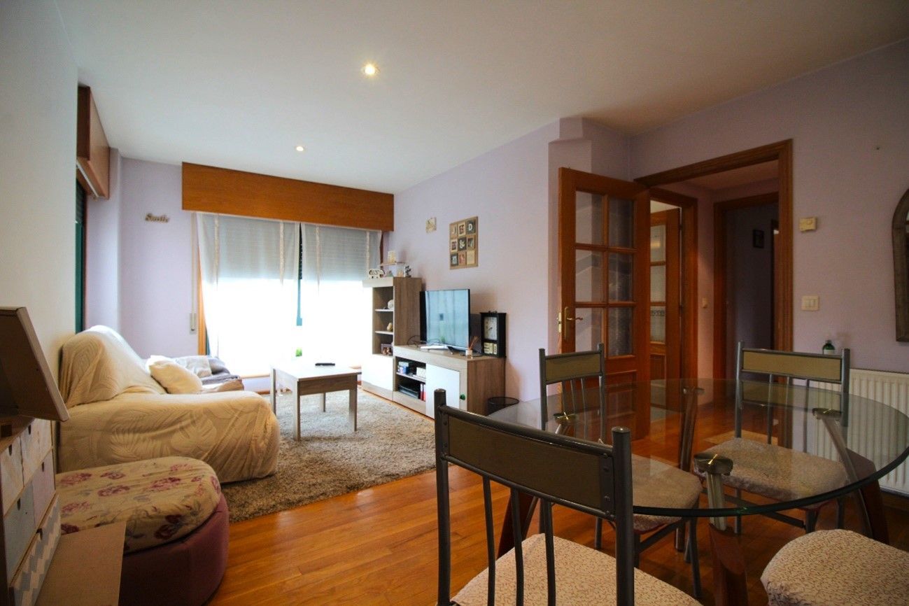 Sala de estar con sofá, TV, comedor y pisos de madera.