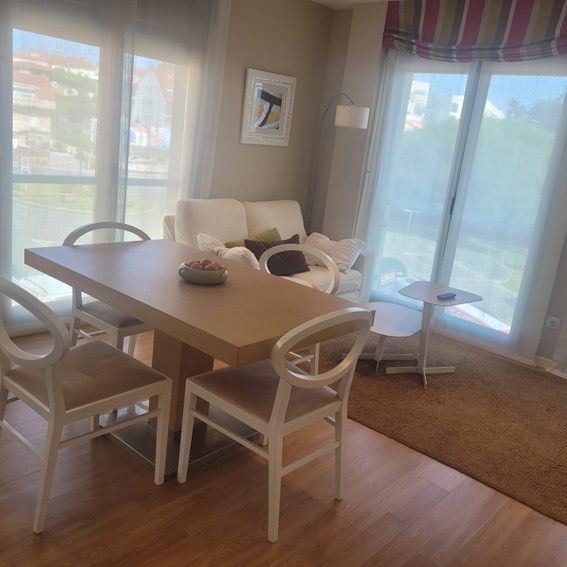 Comedor con mesa, sillas, sofá y grandes ventanales con vistas.