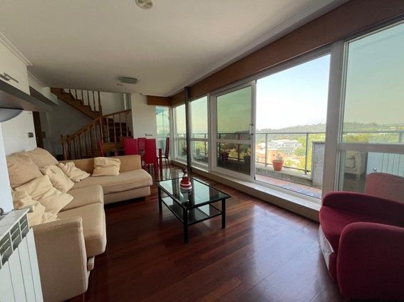 Sala de estar con sofá beige, suelo de madera y grandes ventanales que dan a un balcón.