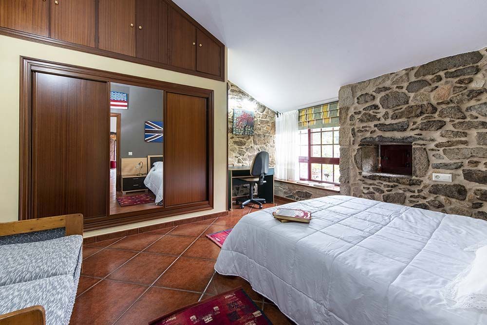 Dormitorio con pared de piedra, cama, escritorio, armario corredizo y suelo de baldosas de terracota.