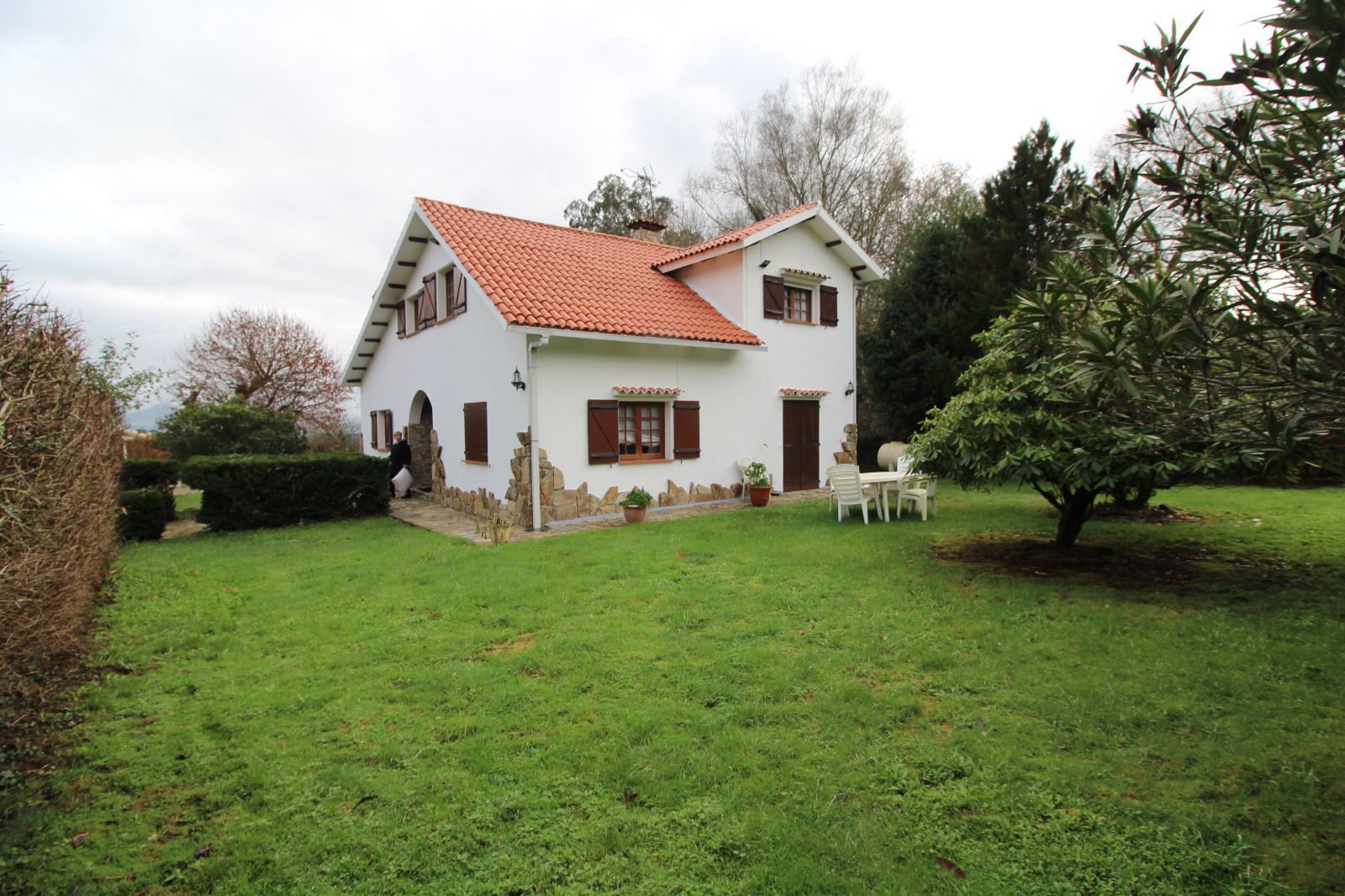 Casa de piedra con techo de tejas rojas y extensión de estuco amarillo. Pequeño patio con césped y muebles de exterior.