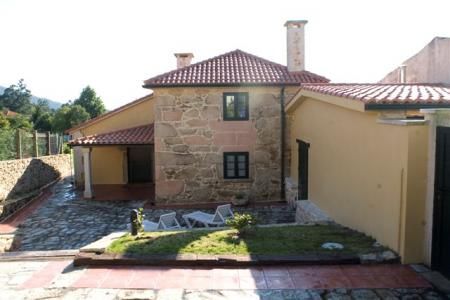Casa de piedra con techo de tejas rojas y extensión de estuco amarillo. Pequeño patio con césped y muebles de exterior.