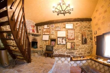 Casa de piedra con techo de tejas rojas y extensión de estuco amarillo. Pequeño patio con césped y muebles de exterior.