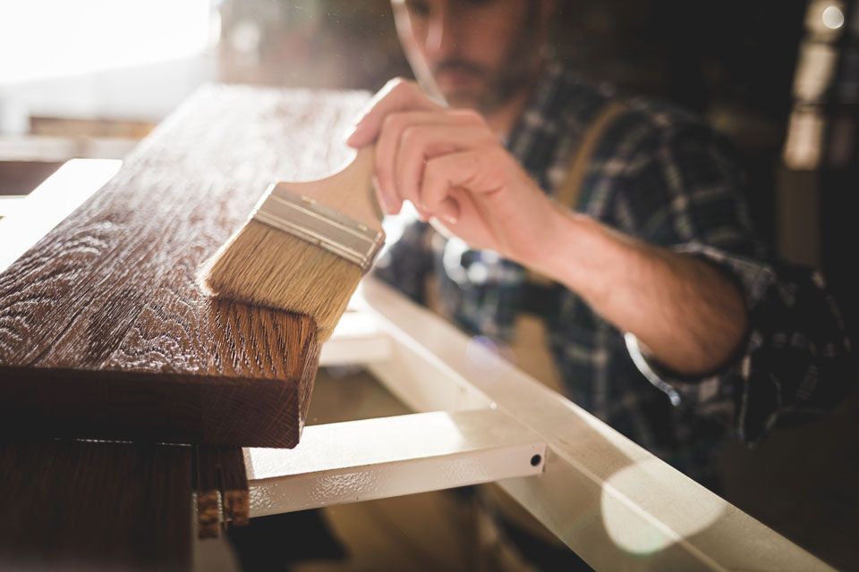 Schreiner lackiert ein Holzstück