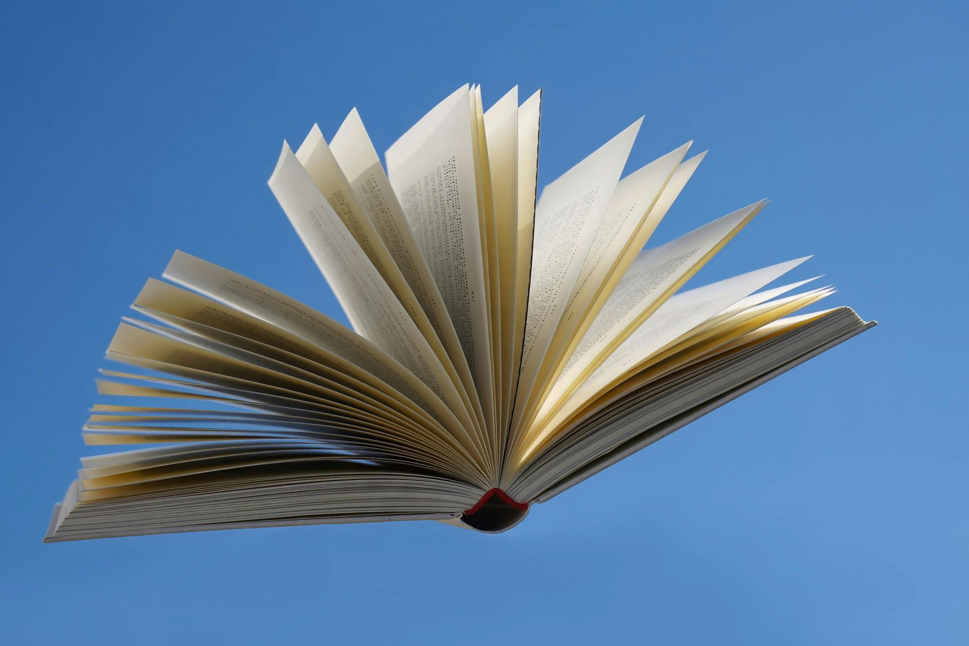 Offenes Buch mit aufgefächerten Seiten, das vor einem strahlend blauen Himmel schwebt.
