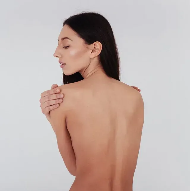 Una mujer sin camisa se sostiene el hombro.