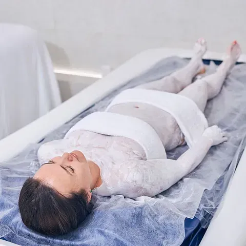 Una mujer está acostada en una cama envuelta en film plástico.
