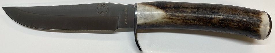 Un cuchillo de hoja fija con hoja oscura y mango de asta reposa sobre una superficie blanca.