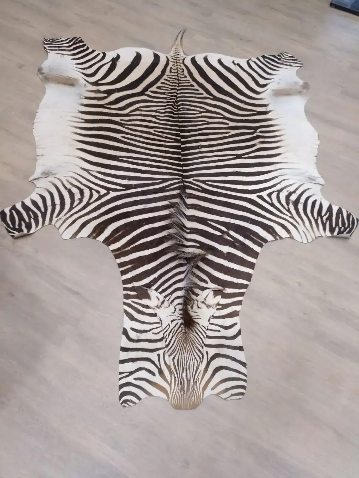 Alfombra de piel de cebra con rayas blancas y negras, colocada sobre un suelo de madera de color claro.