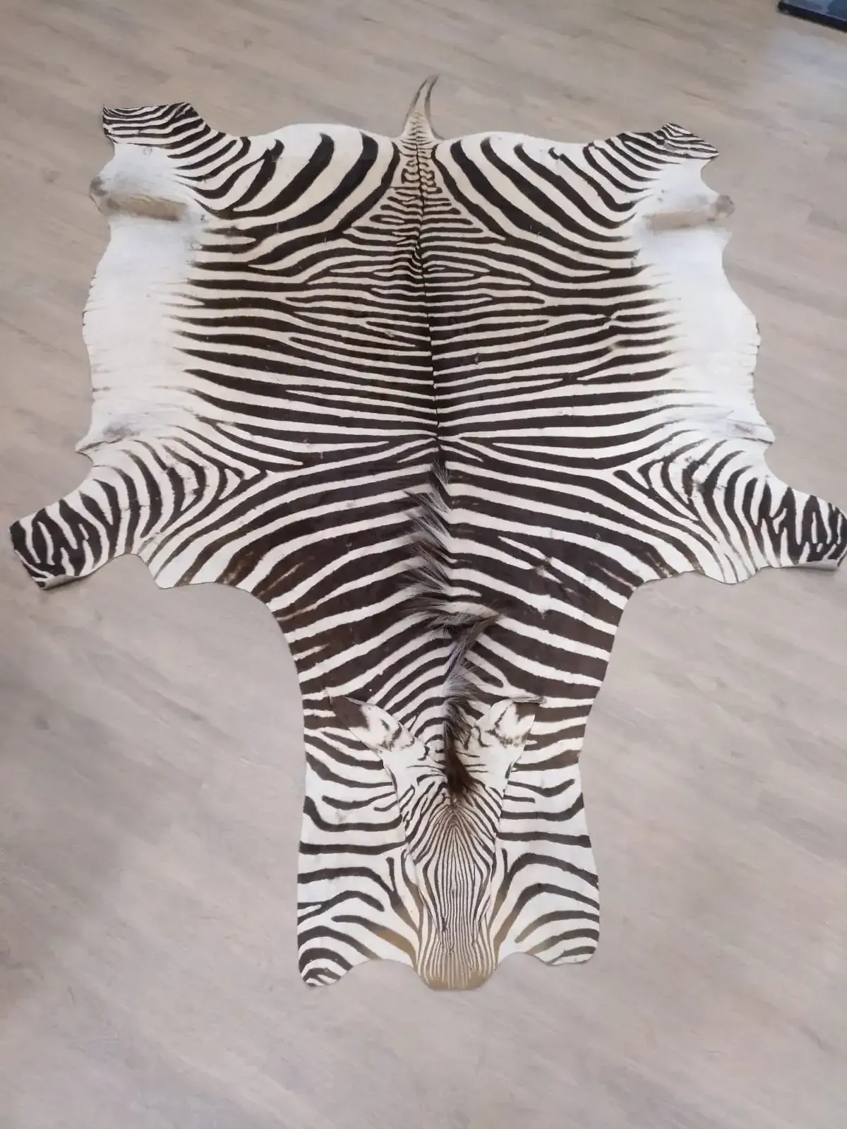 Alfombra de piel de cebra con rayas blancas y negras, extendida sobre un suelo de madera clara.