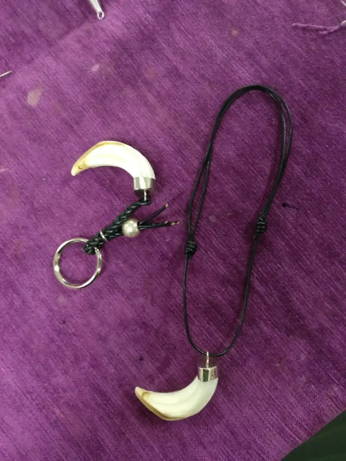 Llavero y collar con colgante de diente curvado de color blanco sobre fondo morado.