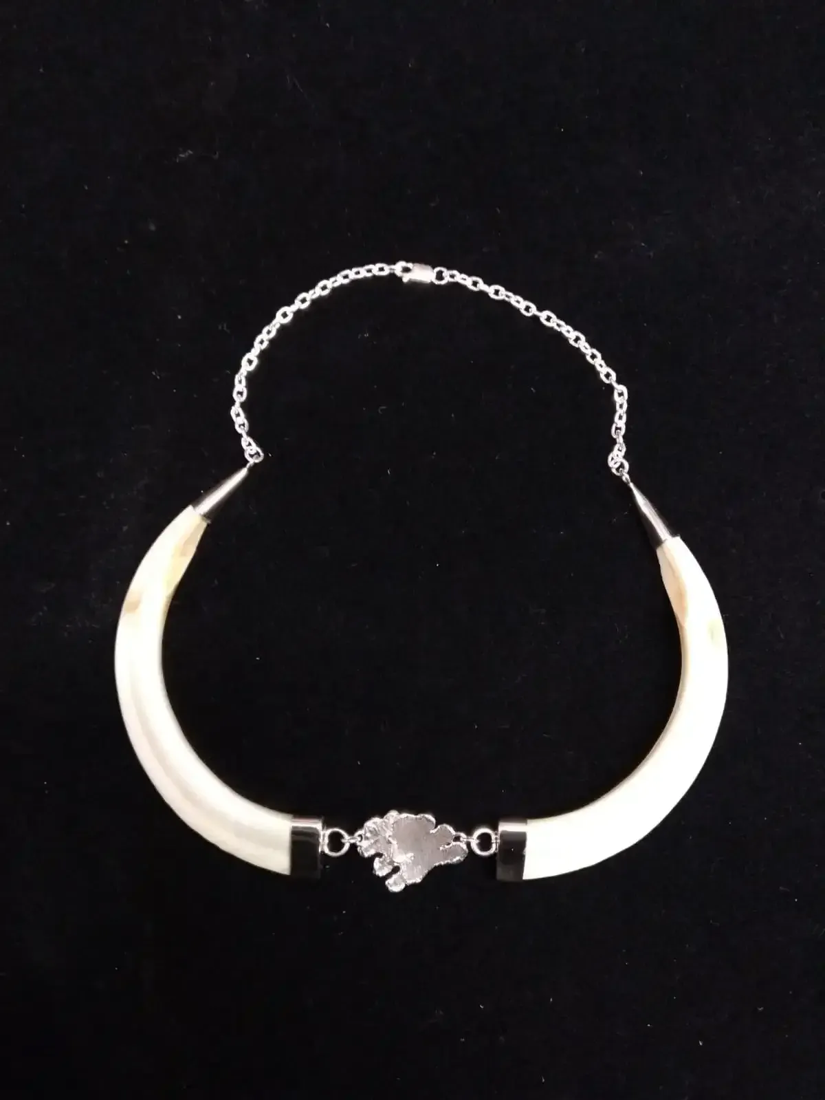 Collar curvo de color crema con cadena y cierre de plata sobre fondo negro.