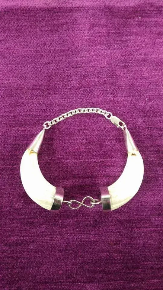 Pulsera colgante curvada de color marfil con cadena de plata sobre superficie violeta.