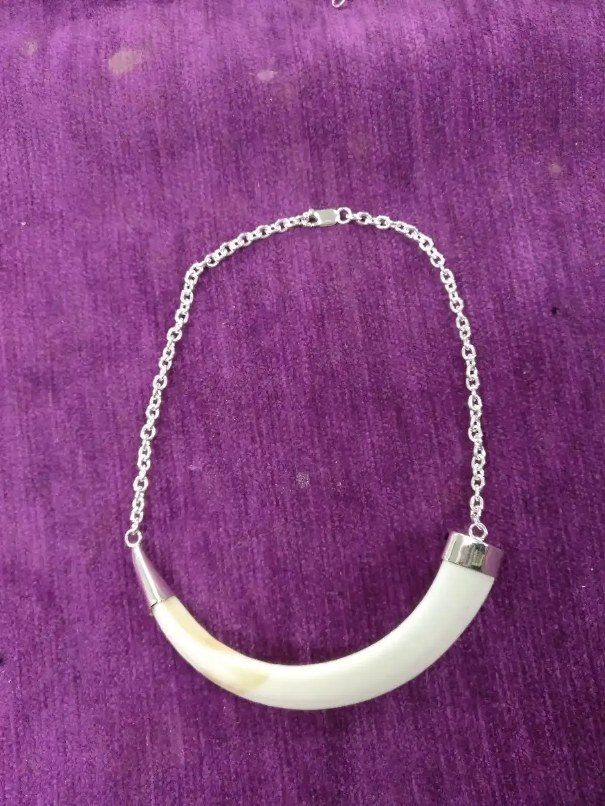 Collar con colgante curvado de color marfil unido a una cadena de plata sobre una tela morada.