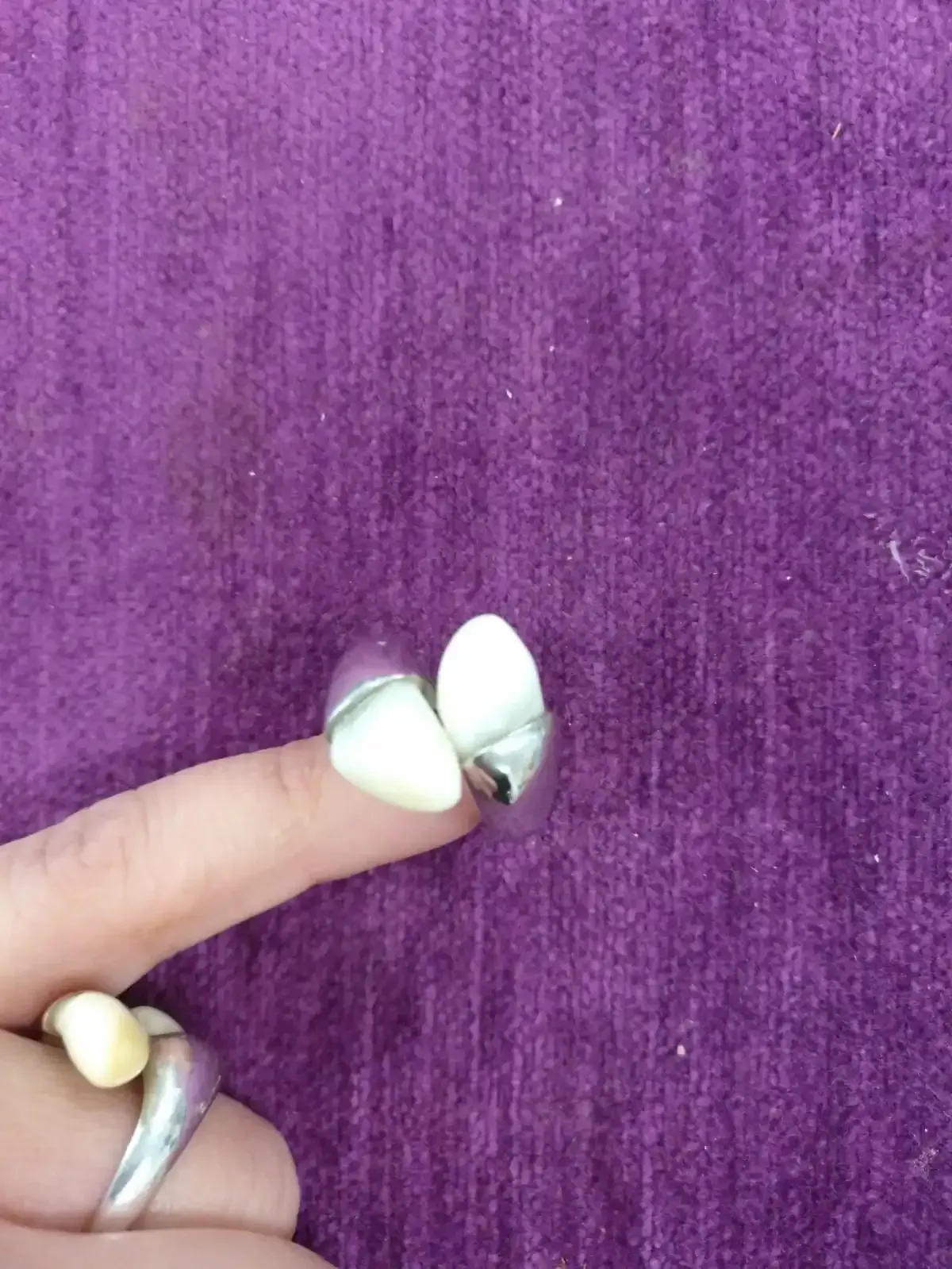 Dedo que lleva un anillo de plata con dos piedras blancas de forma ovalada, engastadas sobre un fondo morado.
