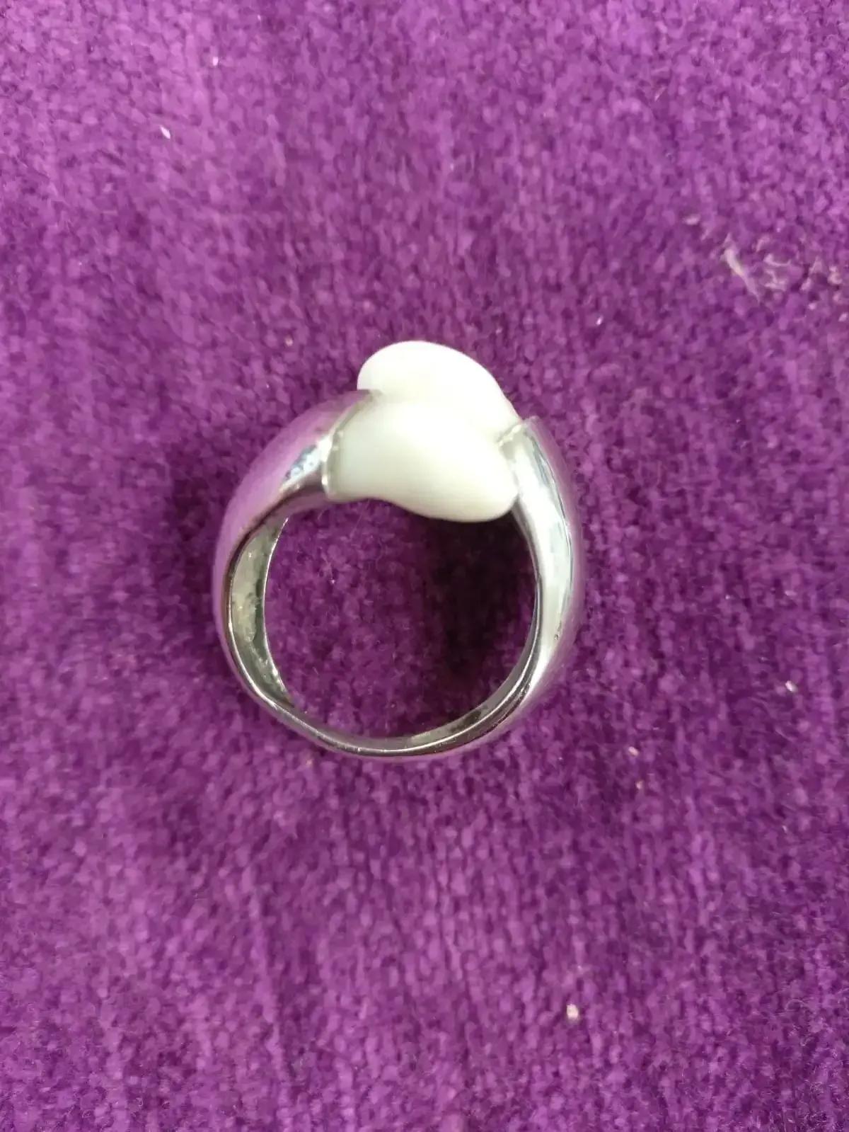 Anillo de plata con centro blanco en forma de diente sobre fondo morado.