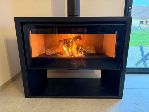 Cheminée noire moderne avec flammes visibles dans une pièce lumineuse, près d'une fenêtre.