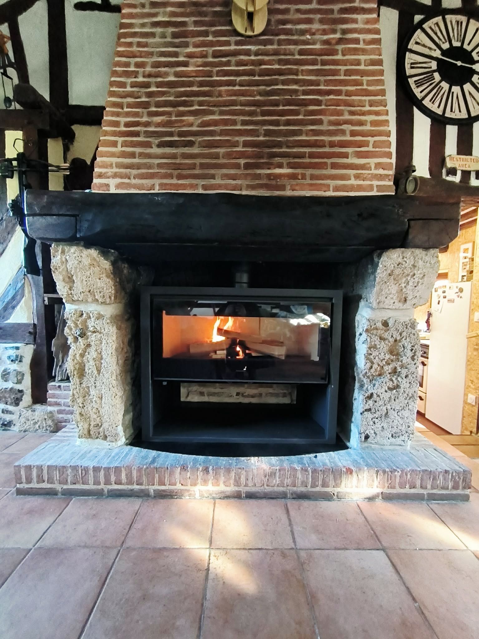 Cheminée en briques avec un feu allumé et un manteau noir dans une pièce rustique.