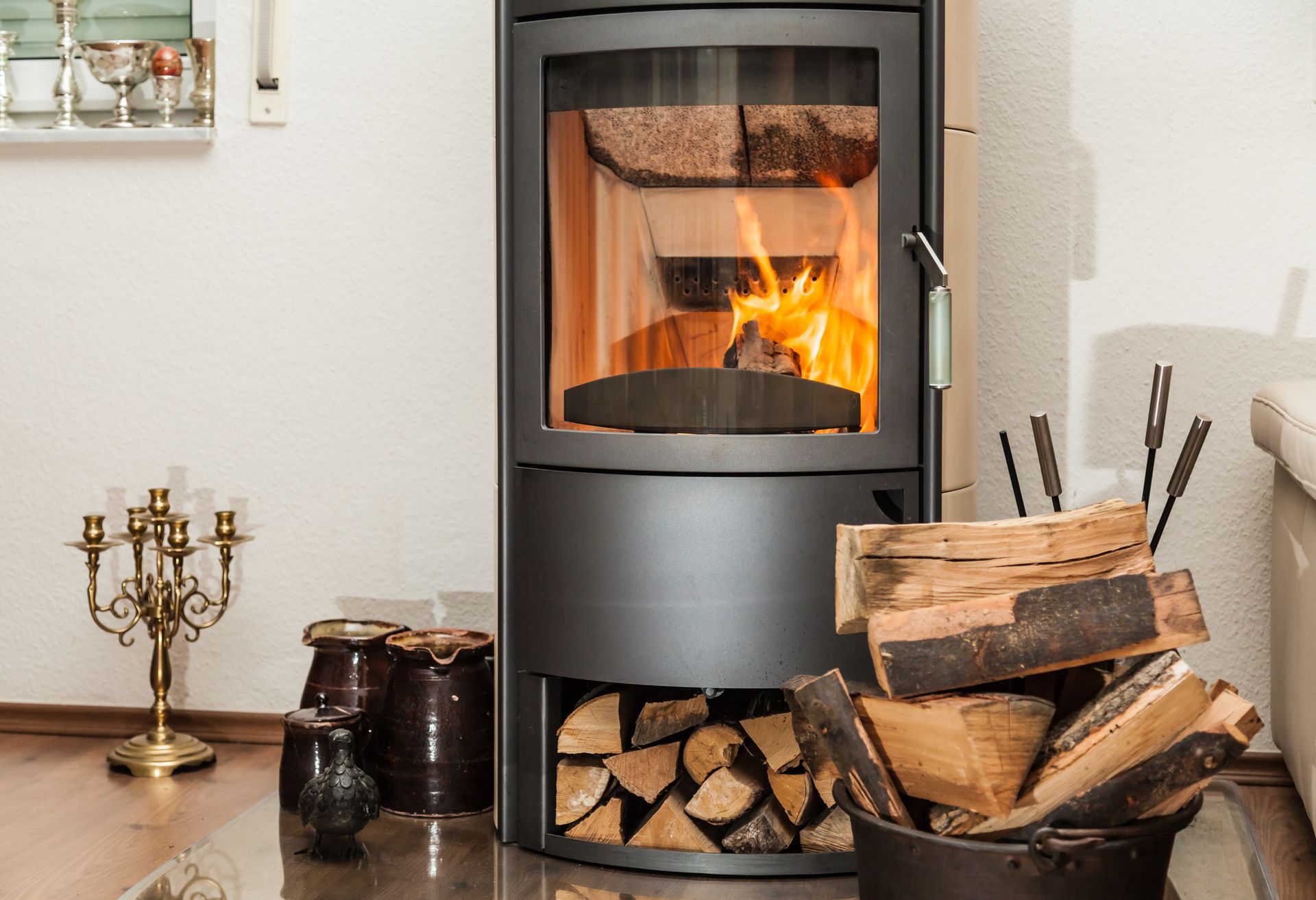 Poêle à bois noir moderne avec un feu allumé, des bûches empilées à côté dans une pièce confortable.