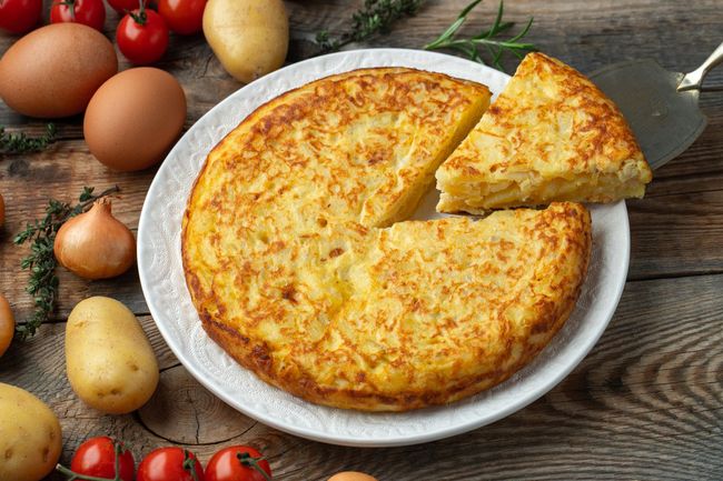 Hay una tortilla en un plato con una rebanada sacada de ella.