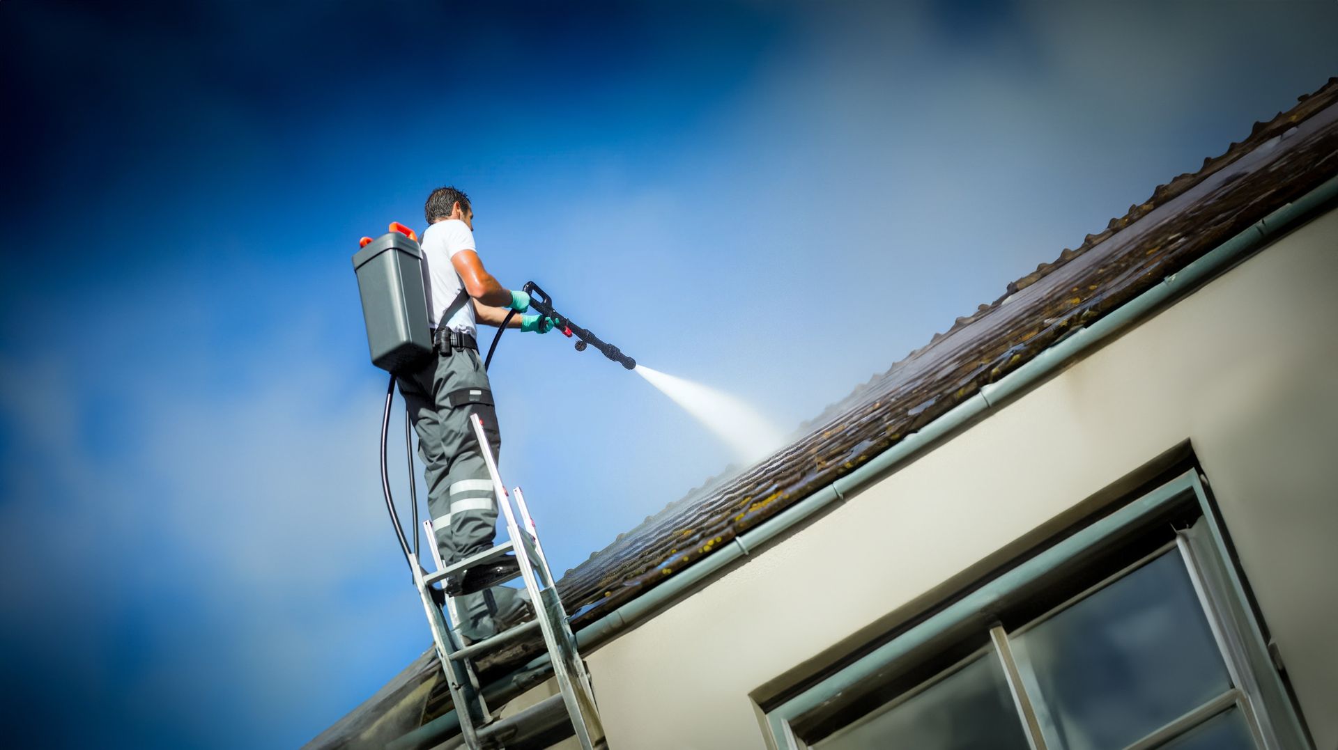Un homme sur une échelle nettoie un toit au nettoyeur haute pression