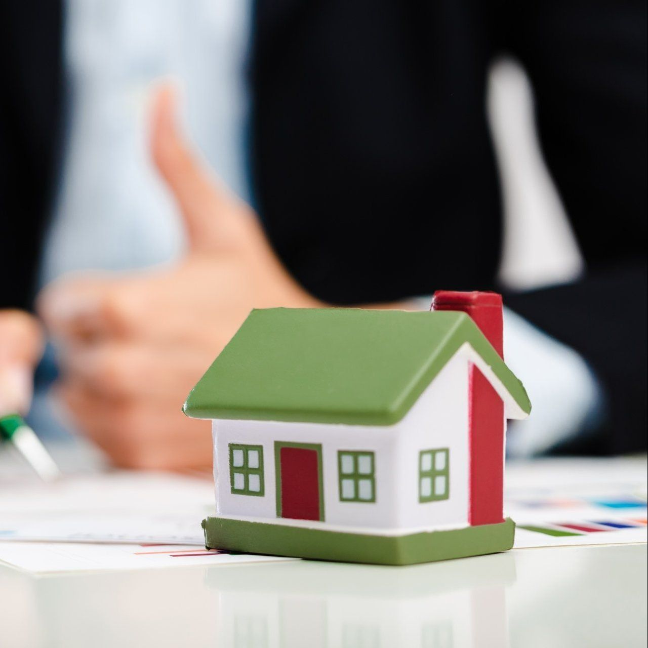 Jouet d'une maison avec toit vert avec en arrière plan flouté un avocat avec le pouce levé