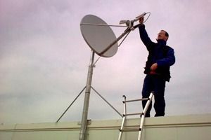 Un hombre está de pie en una escalera al lado de una antena parabólica.