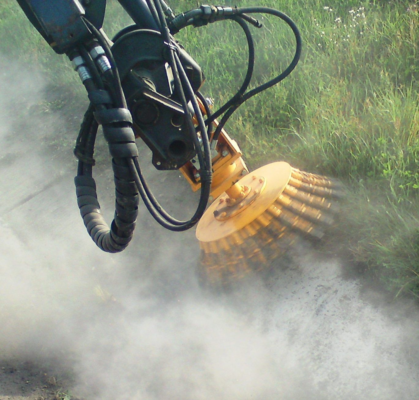L'accessoire de brosse jaune monté sur la machine balaie l'herbe, créant un nuage de poussière.