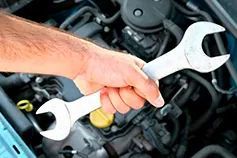 Una persona sostiene dos llaves delante del motor de un automóvil.