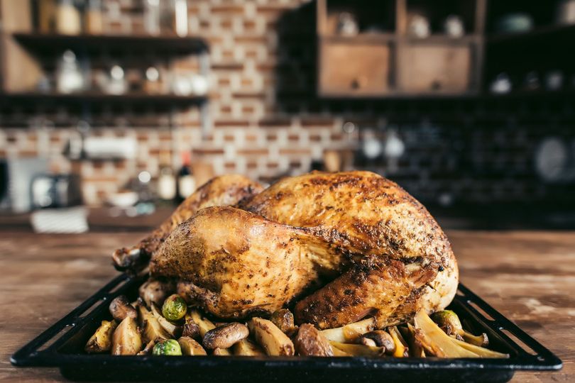 Pavo asado en una bandeja negra con verduras asadas en un entorno de cocina.